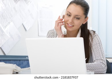 Beautiful Young Business Woman At Work. She Is Talking On A Landline Phone Working On A Laptop.