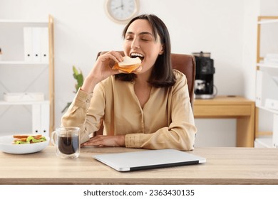 Beautiful young businesswoman eating tasty sandwich at her workplace in office - Powered by Shutterstock