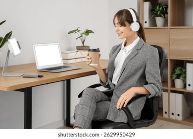 Beautiful young businesswoman in headphones with cup of coffee in office