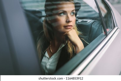 Beautiful young businesswoman sitting on back seat of a car and looking outside the window. Female business executive travelling by a cab.