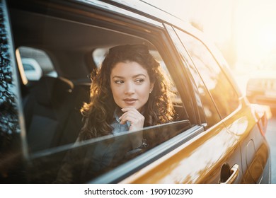 Beautiful young businesswoman sitting on back seat of a car and looking outside the window.