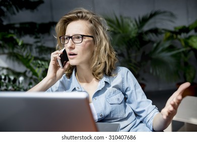 Beautiful Young Businesswoman Using Mobile Phone While Working With Laptop In Office. Upset Or Dissapointed Expression At Her Face