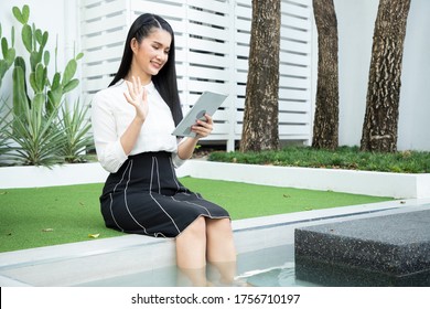 A Beautiful Young Businesswoman Using Tablet And Relaxes Around The Poolside Garden In Front Of The House After She Talk Her Friends By Video Call With Bright Smile.  Working From Home Concept.