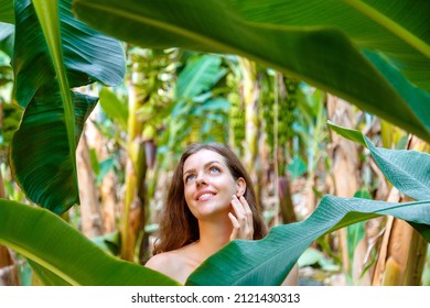 Beautiful Young Caucasian Brunette Long Hair Woman Portrait Near Banana Palm Leaves Tropical Plants In Jungle. Skin Care And Natural Organic Beauty, Personal Care Nature Concept.