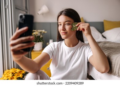 Beautiful Young Caucasian Girl Looks Into Camera Takes Care Of Her Face Skin In Morning. Brown Hair Woman Sitting On Floor At Home. Concept Beauty, Gadgets.