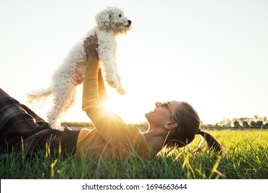 Beautiful young caucasian girl playing with her dog lying on the grass in the park at sunset. Animal, friendship, people and love concept