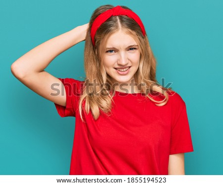 Beautiful young caucasian girl wearing casual red t shirt confuse and wonder about question. uncertain with doubt, thinking with hand on head. pensive concept. 