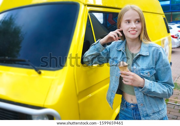 Beautiful Young caucasian Lady eat Ice Cream in front of\
ice cream van. Woman standing with ice-cream before an yellow old\
hippie bus. 