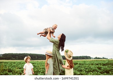 Beautiful young caucasian mother with children in a linen dress with a basket of strawberries gathers a new crop and has fun with the children - Powered by Shutterstock