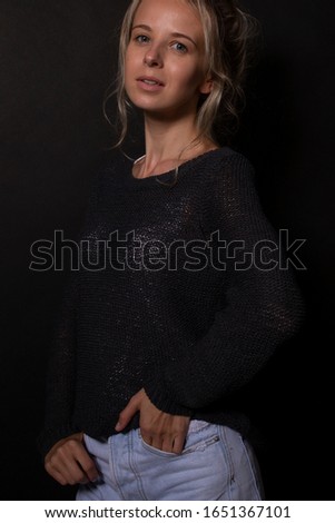 Beautiful young caucasian woman with blond bunched hair and clear no makeup skin posing for photoshoot. Smiles playfully. Black background. Portrait shoot in professional studio.