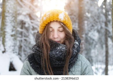 A Beautiful Young Caucasian Woman With Closed Eyes And A Smile On Her Face Relaxes And Enjoys The Sun And Air At Sunset In A Winter Coniferous Forest. Warmly Dressed Girl In The Forest.