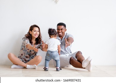 Beautiful young Caucasian woman couple and an African American man are pulling their hands to their charming mixed race daughter. Concept of posing on white background. Copyspace