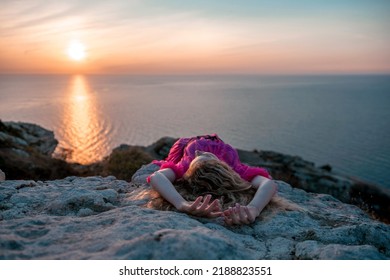 Beautiful young caucasian woman with curly blond hair and freckles. Cute redhead woman portrait in a pink long dress posing on a volcanic rock high above the sea during sunset.