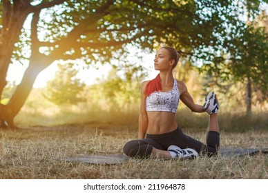 Beautiful Young Caucasian Woman In Fitness Wear Doing Exercises In A Park