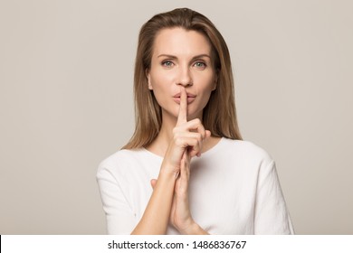 Beautiful Young Caucasian Woman Isolated On Grey Studio Background Hold Finger At Lips Ask Be Silent Quiet, Millennial Female Look At Camera Tell Share Mystery, Announce Secret Sale Or Discount