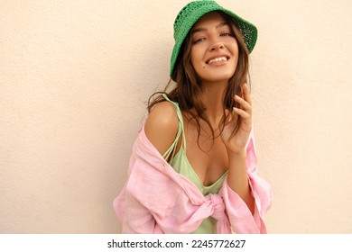 Beautiful young caucasian woman looking at camera wide smiling during summer day. Model with brunette wavy hair wears shirt and sundress. Concept of great mood.