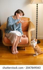 Beautiful Young Caucasian Woman With Short Hair Dressed In Skirt And Knitted Sweater Plays With Cat With Mouse On String.