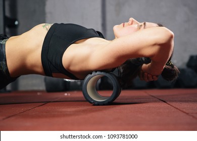Beautiful young caucasian woman sportswoman uses a foam roller massager for relaxation, stretching muscles and back pain. Girl in the gym green sneakers T-shirt and tights.