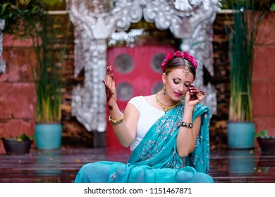 Beautiful young caucasian woman in traditional indian clothing sari with bridal makeup and jewelry and henna tattoo on hands dancing in temple garden.