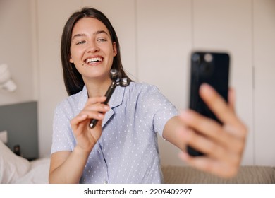 Beautiful Young Caucasian Woman With Wide Smile Shows Her Face Massager For Subscribers . Brunette Hair Girl Using Internet On Phone. Concept Beauty, Gadgets.