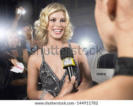 Beautiful young celebrity being interviewed by journalist at premiere