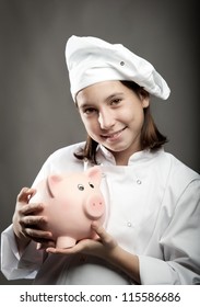 Beautiful Young Chef  Holding A Piggy Bank On Gray Background