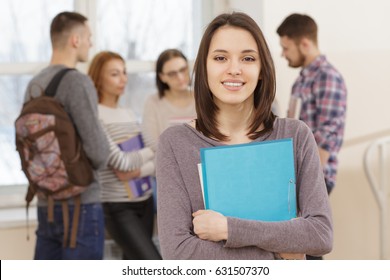 Beautiful young college student standing in front of her friends in the hallway smiling to the camera holding her books copyspace education togetherness relationships friendship study campus concept - Powered by Shutterstock