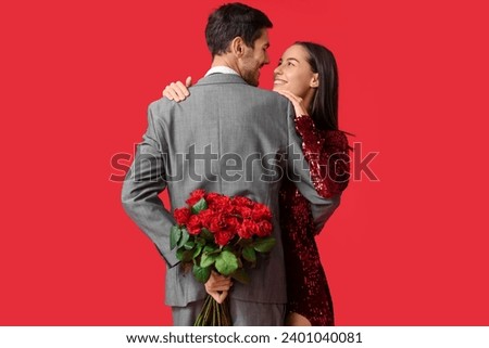Beautiful young couple with bouquet of roses on red background. Valentine's day celebration