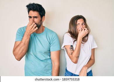 Beautiful Young Couple Of Boyfriend And Girlfriend Together Smelling Something Stinky And Disgusting, Intolerable Smell, Holding Breath With Fingers On Nose. Bad Smell 