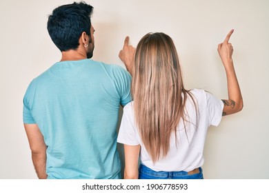 Beautiful young couple of boyfriend and girlfriend together posing backwards pointing ahead with finger hand 