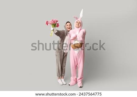 Beautiful young couple in bunny costume with Easter basket and bouquet of tulips on grey background