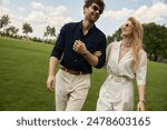 A beautiful young couple dressed in elegant clothing enjoys a leisurely walk in the park on a green field, embodying old money style and rich people lifestyle.