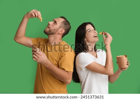 Beautiful young couple eating french fries on green background