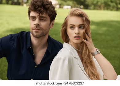 A beautiful young couple in elegant attire sitting on a verdant grassy field, embodying a luxurious and carefree lifestyle. - Powered by Shutterstock