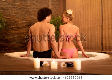 Beautiful young couple enjoying in a jacuzzi at the spa center. Rear view.