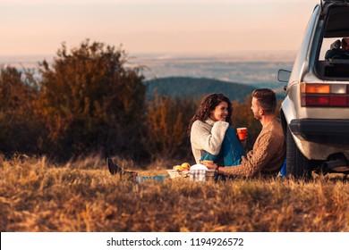 Beautiful young couple enjoying picnic time on the sunset. They drinking tea and sitting in a meadow.