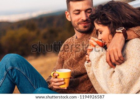 Beautiful young couple enjoying picnic time on the sunset. They drinking tea and sitting in a meadow.