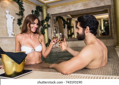 Beautiful young couple enjoying and relaxing in SPA center. They sitting in jacuzzi and drinking wine.