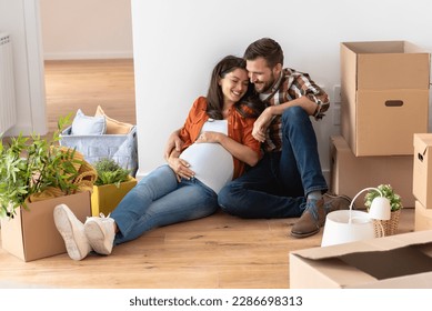 Beautiful young couple expecting a baby just moved into an empty apartment, sitting among cardboard boxes making plans for future. New beginnings - Powered by Shutterstock