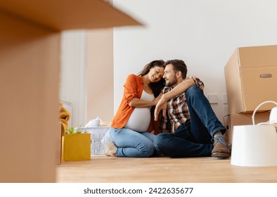 Beautiful young couple expecting a baby just moved into an empty apartment, sitting among cardboard boxes making plans for future. New beginnings - Powered by Shutterstock