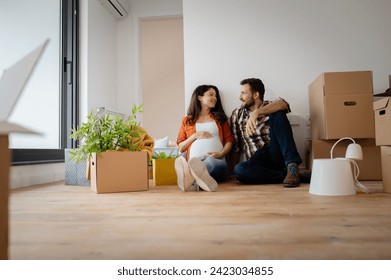 Beautiful young couple expecting a baby just moved into an empty apartment, sitting among cardboard boxes making plans for future. New beginnings - Powered by Shutterstock