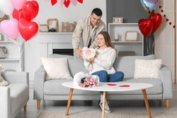 Beautiful Young Couple With Gift Box, Bouquet Of Flowers And Heart-shaped Balloons Celebrating Valentine's Day At Home