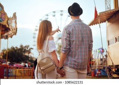 Beautiful, young couple having fun at an amusement park. Couple Dating Relaxation Love Theme Park Concept. Couple posing together on the background of a ferris wheel. Tourists have fun, smile.