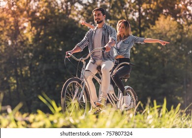 Beautiful young couple is having fun while riding a tandem bicycle in the park - Powered by Shutterstock