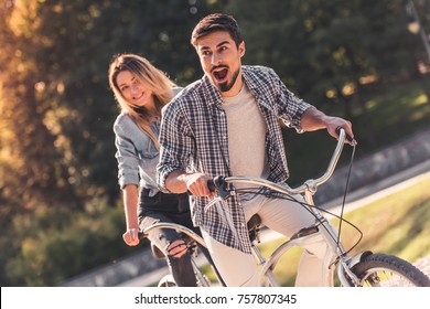 Beautiful young couple is having fun while riding a tandem bicycle in the park - Powered by Shutterstock