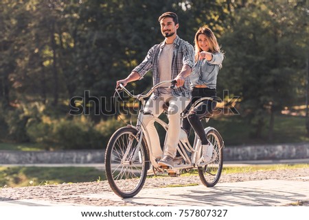 Beautiful young couple is having fun while riding a tandem bicycle in the park