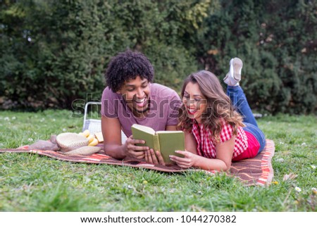 Beautiful young couple having picnic happy about nice weather lying on green grass