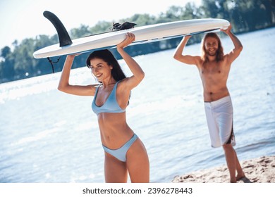 Beautiful young couple is holding a paddle board overhead and smiling while resting on the beach - Powered by Shutterstock