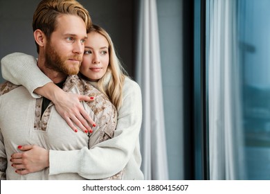 Beautiful Young Couple Hugging And Looking Out Window Indoors