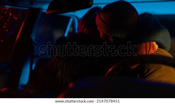Beautiful Young Couple Kissing in the\
Darkness in an Old Looking Car with Neon Light Contrasting the\
Photo, Warm Street Light Hitting from the\
Window.
